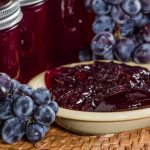 Grape jelly in a bowl with grapes surrounding bowl.