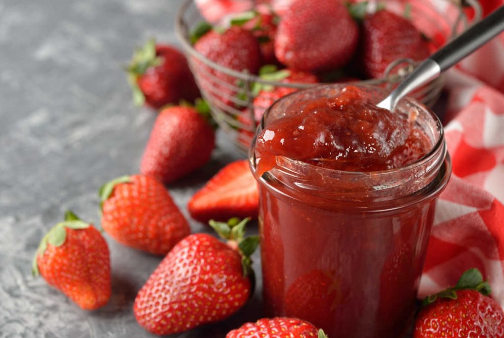 Mason jar with strawberry jam and strawberries around the outside of it.