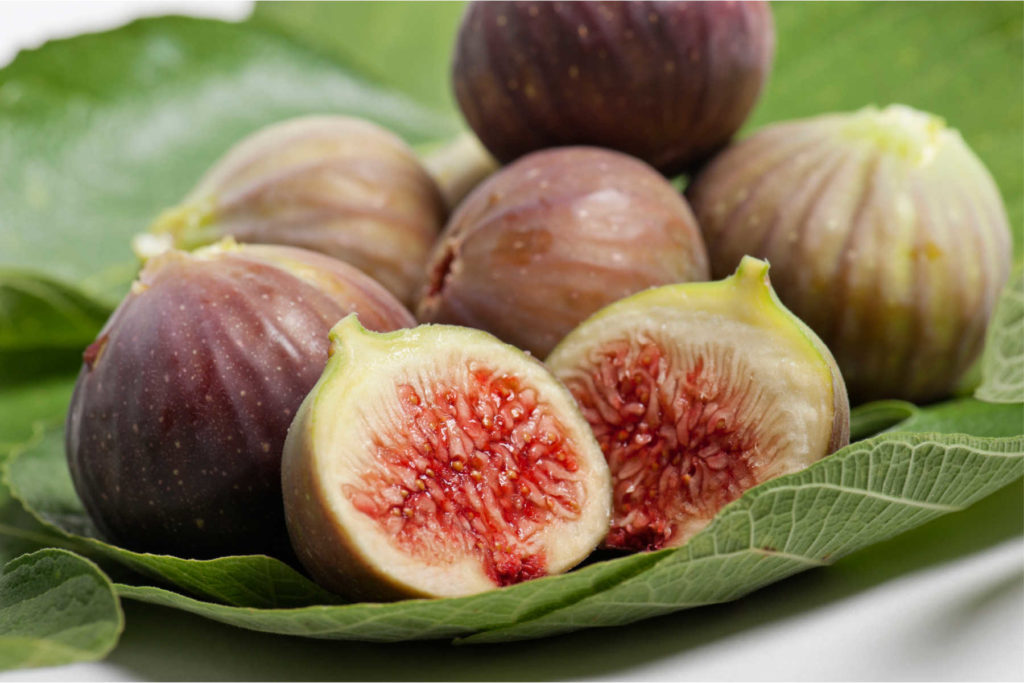 Figs on a leaf with the closest fig cut open.